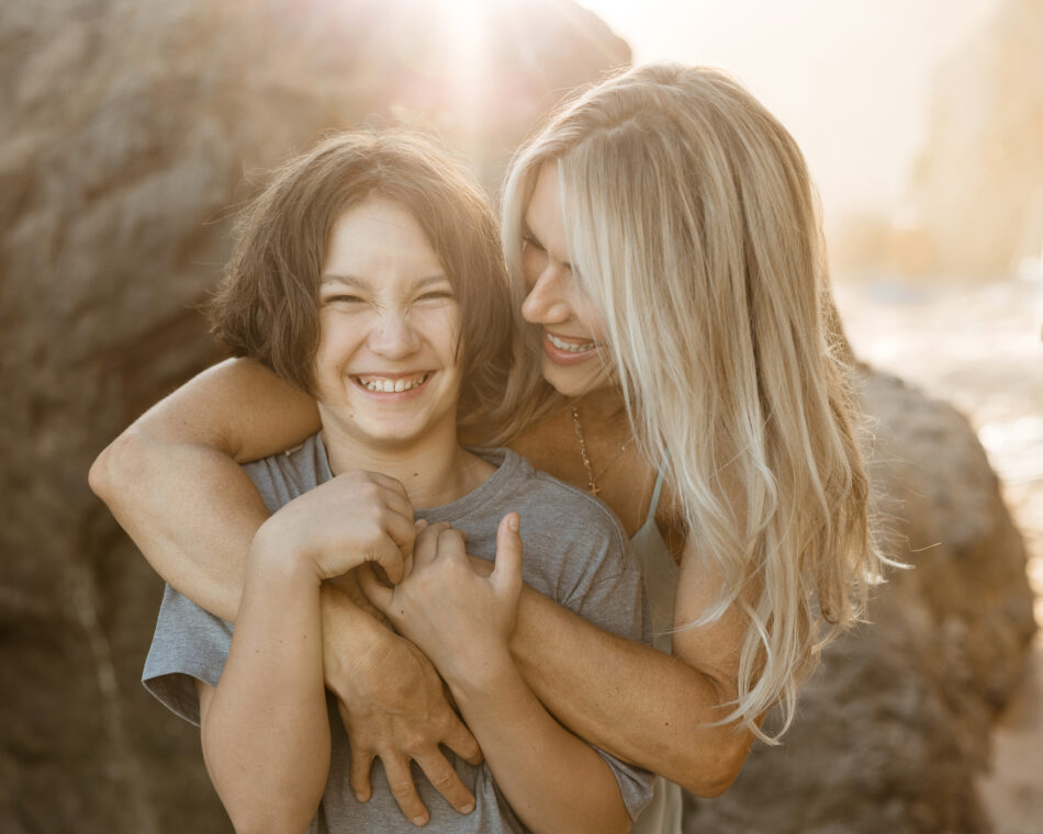 Mother hugging her laughing son during a golden hour family photography session at El Matador Beach in Malibu photographed by Erica Montgomery.