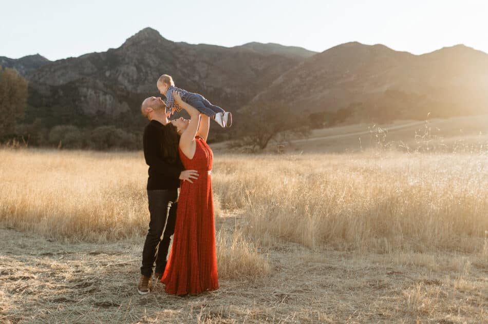 Parents lifting baby in golden field at Malibu Creek State Park in California during sunset