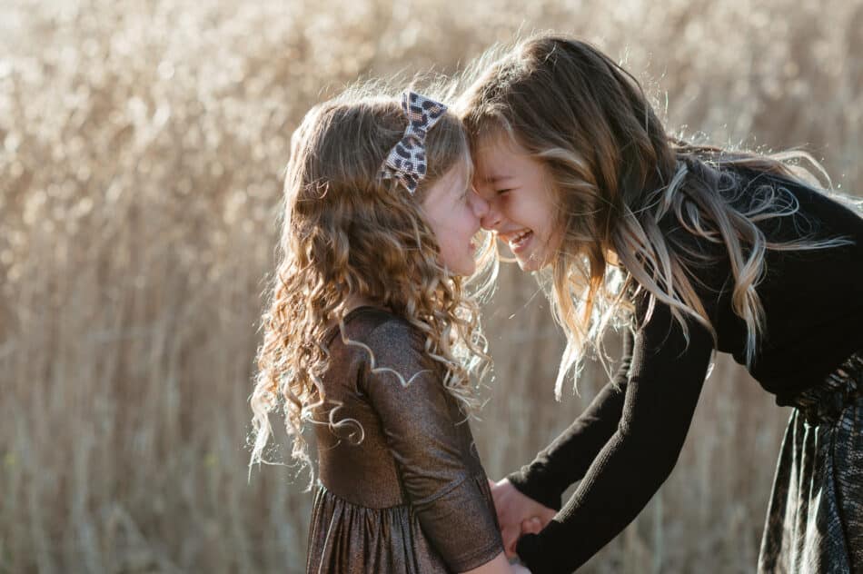 Two young sisters laughing and touching foreheads during a golden hour family session at Malibu Creek