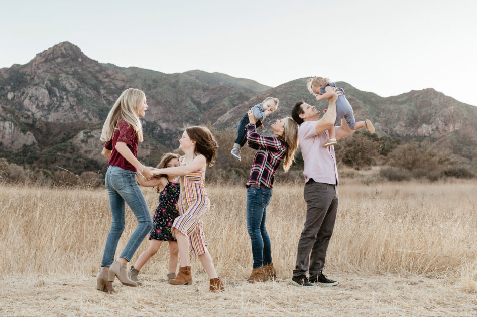 Malibu Creek family photography session with parents lifting young children in golden field with Santa Monica Mountains behind