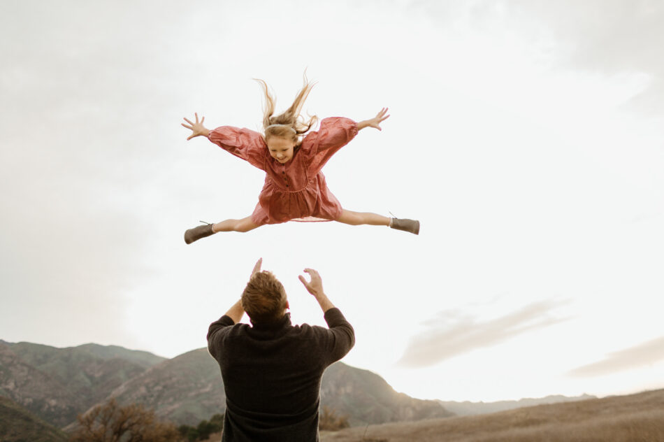 Father tossing daughter into the air during a golden hour family photography session at Malibu Creek State Park near Calabasas photographed by Erica Montgomery.