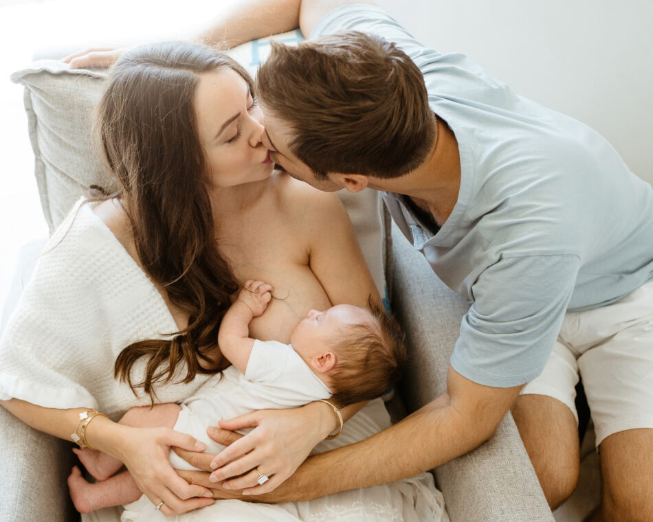 Mother breastfeeding her newborn baby while father leans in to kiss her during an in-home newborn photography session in Woodland Hills photographed by Erica Montgomery.