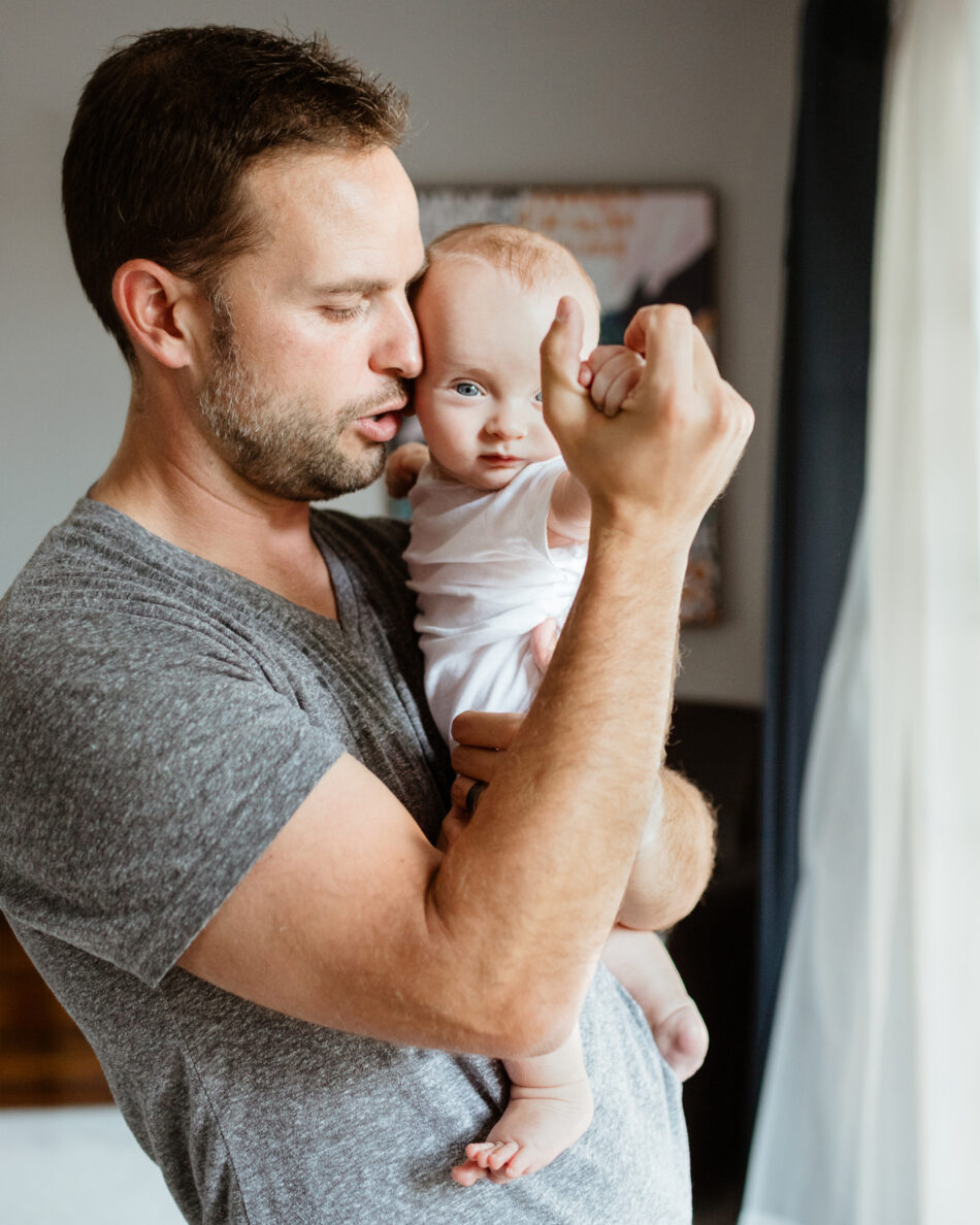 Father holding and kissing his newborn baby during an in-home lifestyle newborn session photographed by Los Angeles family photographer Erica Montgomery.