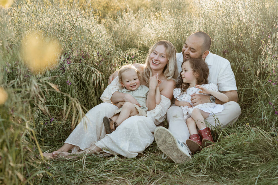 Family of four sitting together in tall grass during a golden hour Malibu Creek family photography session