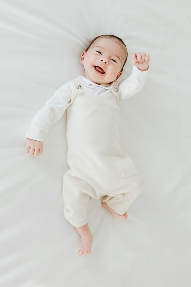Happy newborn baby smiling while laying on a white bed sheet during a lifestyle portrait session in Calabasas by Erica Montgomery Photography.