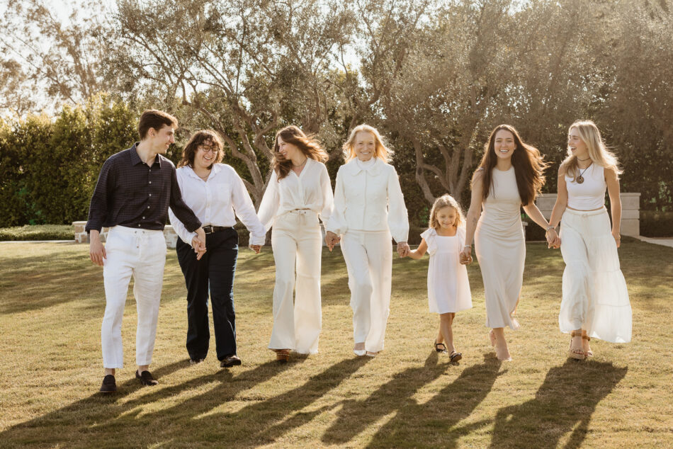 Candid In-home extended family portrait of an extended family walking hand-in-hand across a sun-drenched grassy lawn in Malibu, California.

