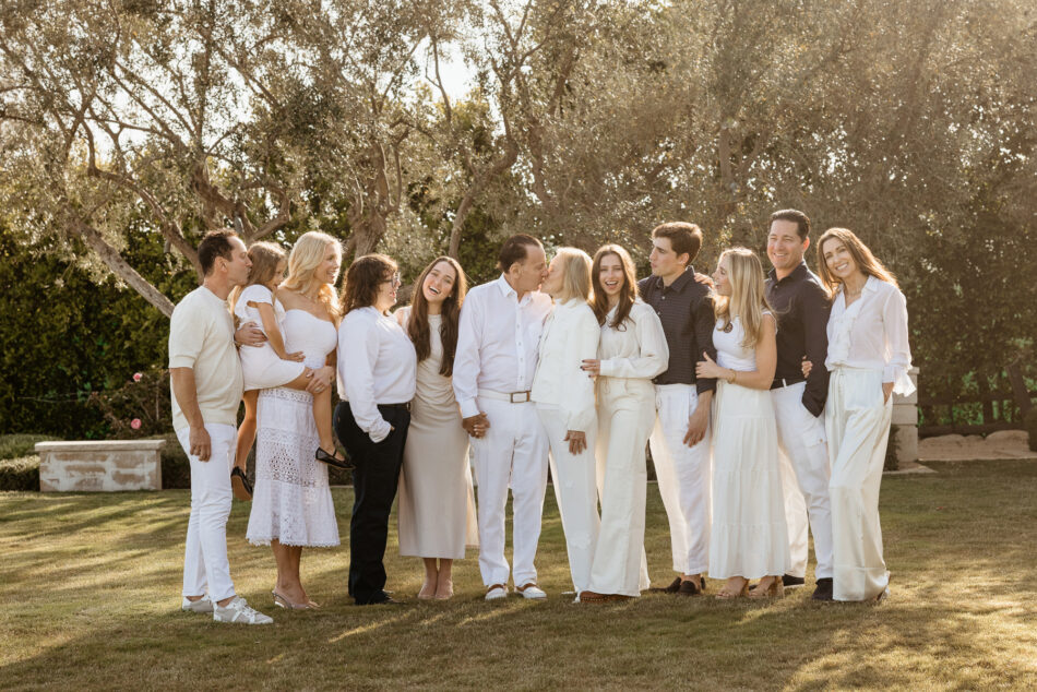 In-home extended family portrait of family wearing all-white outfits posing together in their grassy backyard surrounded by trees in Malibu, California.
