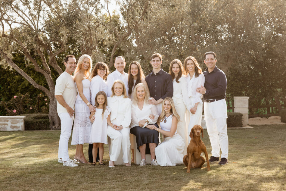 Extended family smiling together on a grassy lawn with a Vizsla dog during a luminous backyard Malibu family photography shoot.
