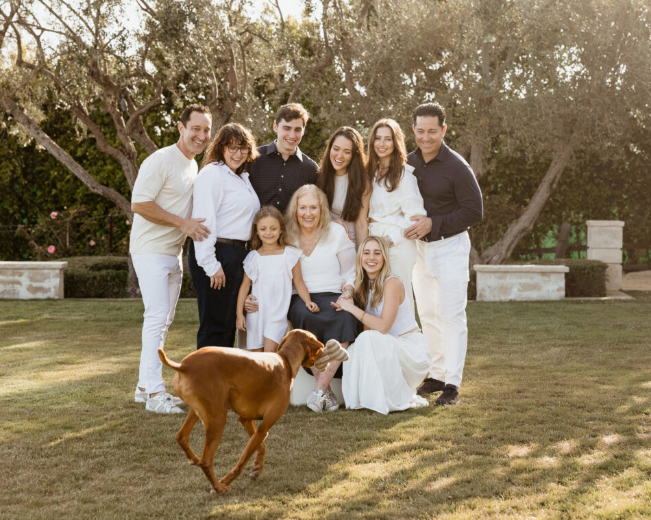 Large multi-generational family wearing coordinated white outfits posing together with their dog during a Malibu backyard session.
