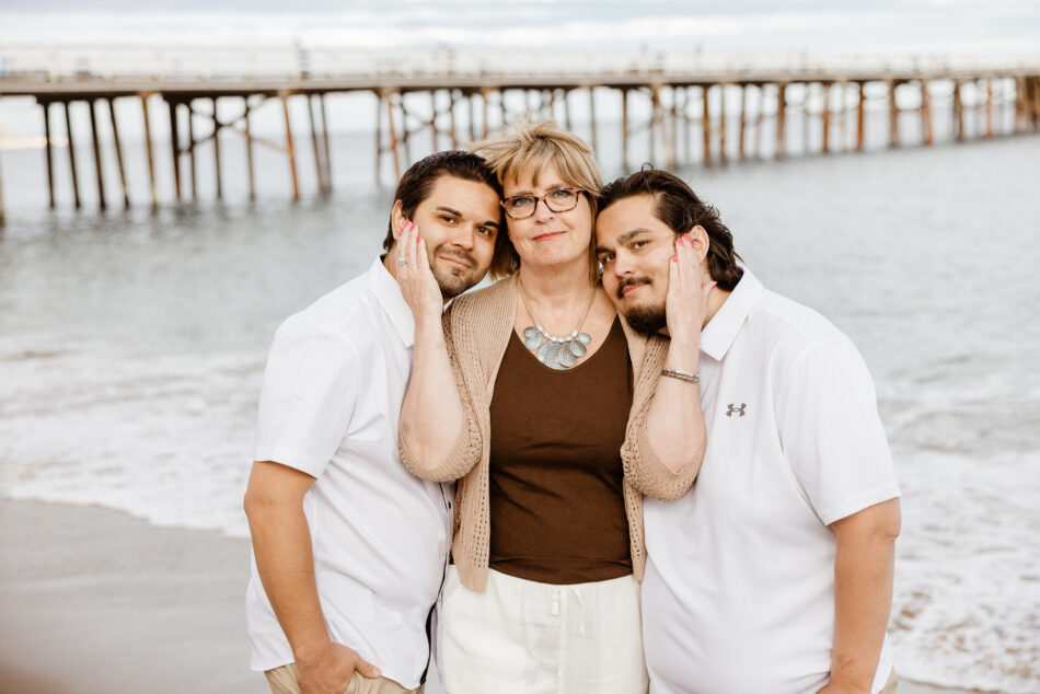 Intimate portrait of a mother posing with her two adult sons on the beach near the Malibu Pier.
