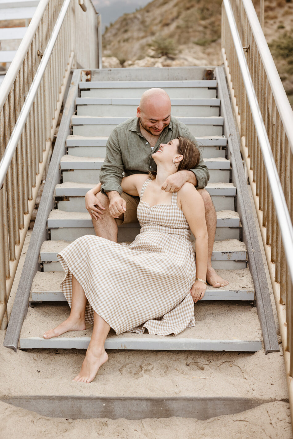 Engaged couple cuddling on wooden beach stairs during a sunset engagement session at El Matador State Beach by Erica Montgomery Photography.