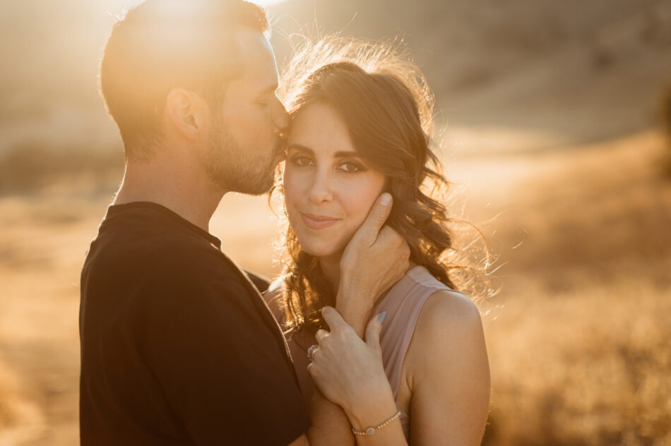 Man kissing his fiancée's hand by iconic sea caves during an El Matador State Beach proposal session by Erica Montgomery Photography.