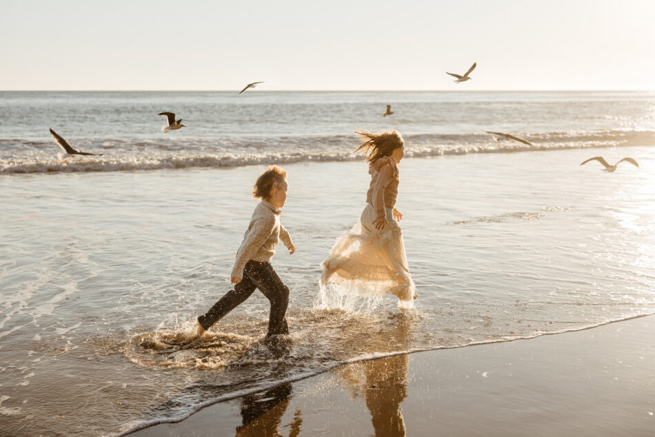 Children running along the shoreline at Malibu beach during golden hour, captured in natural light by Erica Montgomery Photography