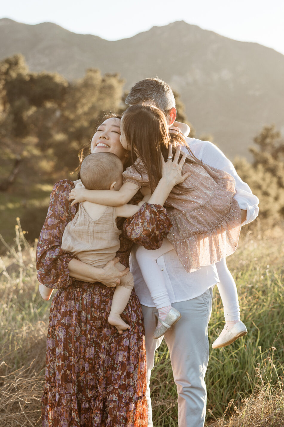 Mother smiling during a big family group hug with her husband and two young children in a Malibu mountain canyon field by Erica Montgomery Photography.