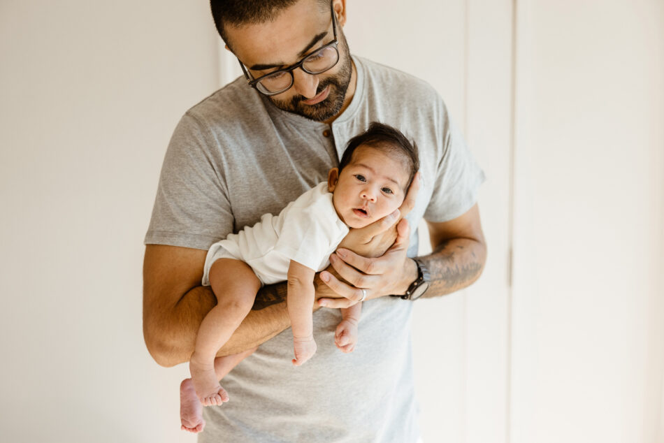 Father with glasses holding his awake newborn baby girl during an all-inclusive lifestyle home session in Calabasas by Erica Montgomery Photography.