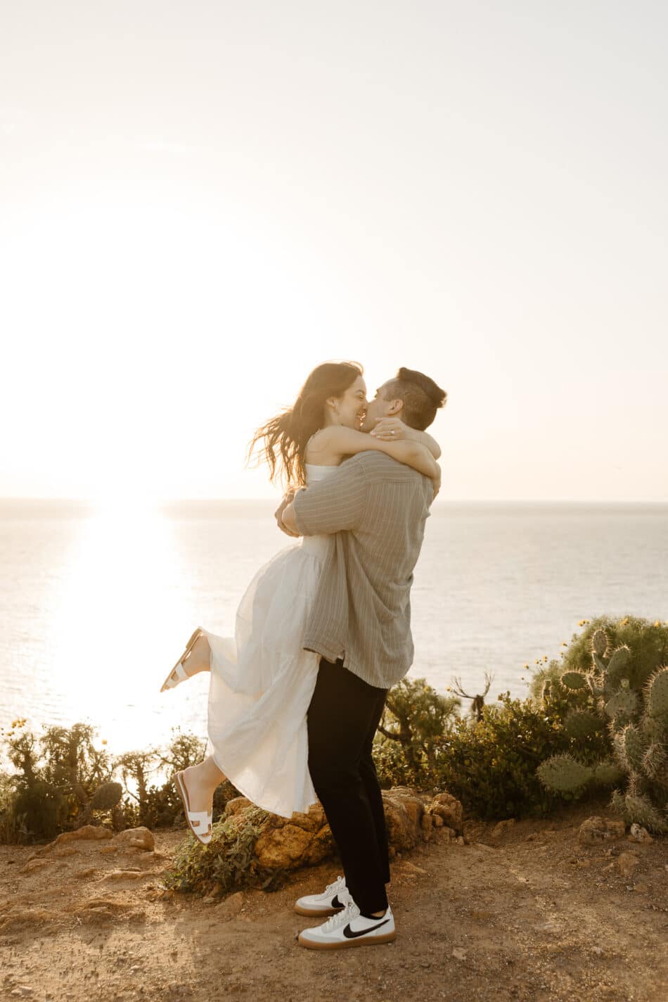 Newly engaged couple hugging and kissing at golden hour during a Malibu cliffside proposal by Erica Montgomery Photography.