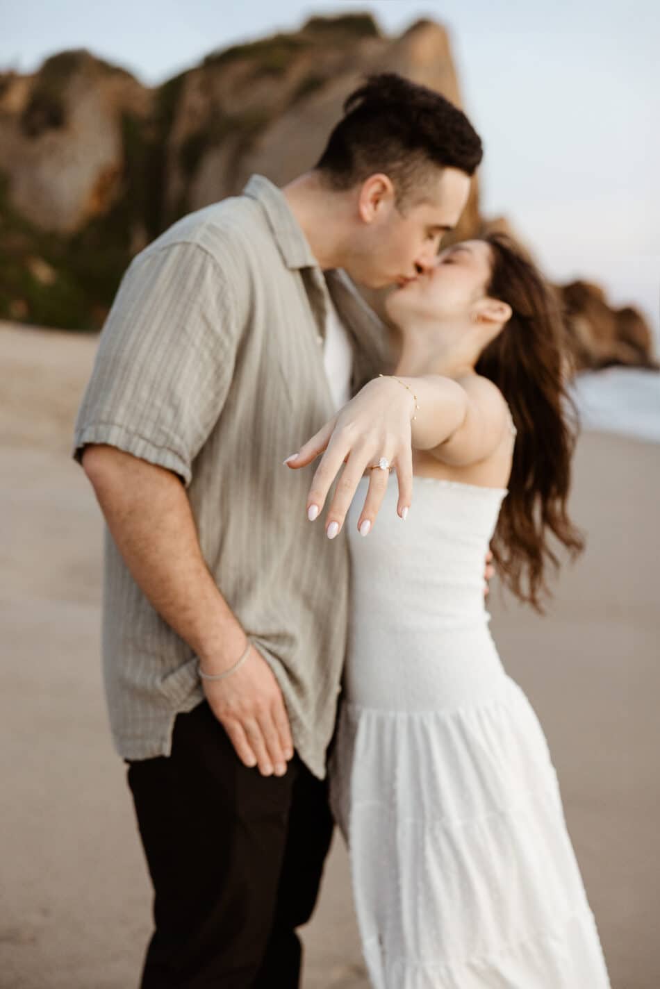 Engaged couple kissing on the beach with a close-up focus on the diamond ring during an El Matador State Beach proposal by Erica Montgomery Photography.