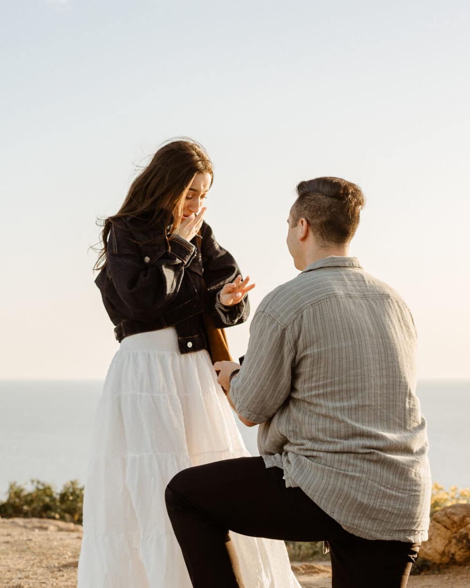 Man down on one knee proposing to surprised woman on a cliffside overlook in Malibu by Erica Montgomery Photography.