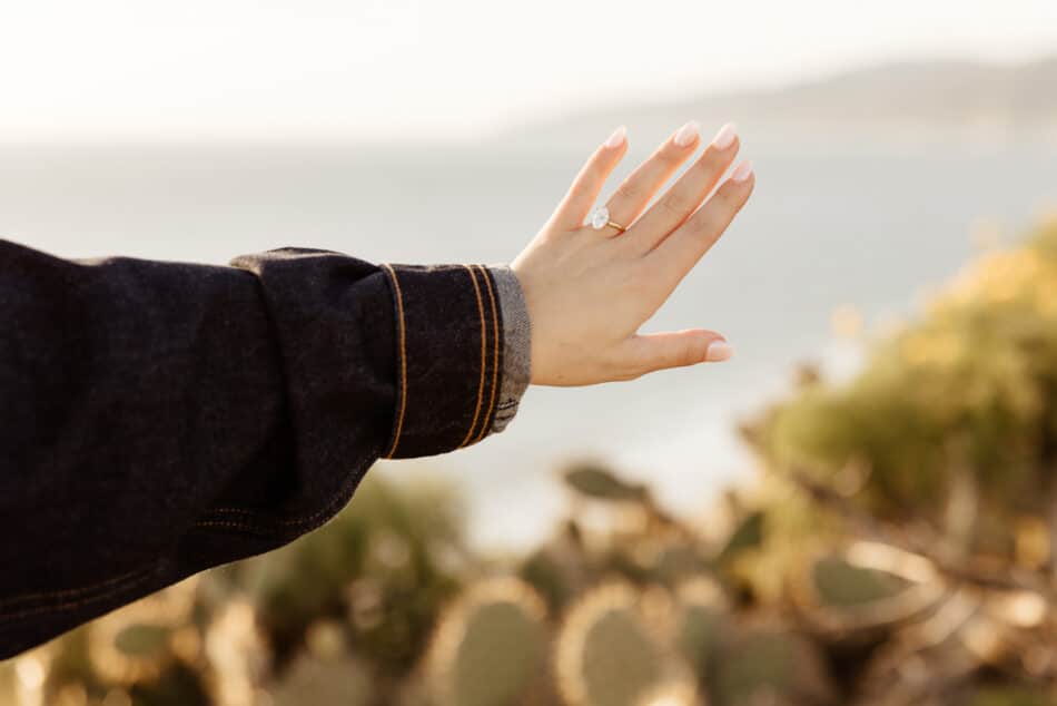 Close-up of an oval diamond engagement ring on a woman's hand at a Malibu coastal proposal by Erica Montgomery Photography.