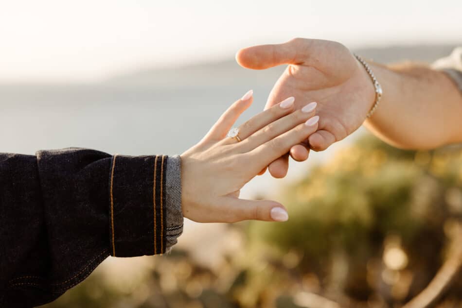 Close-up of a couple holding hands showing an engagement ring at a Malibu beach proposal by Erica Montgomery Photography.