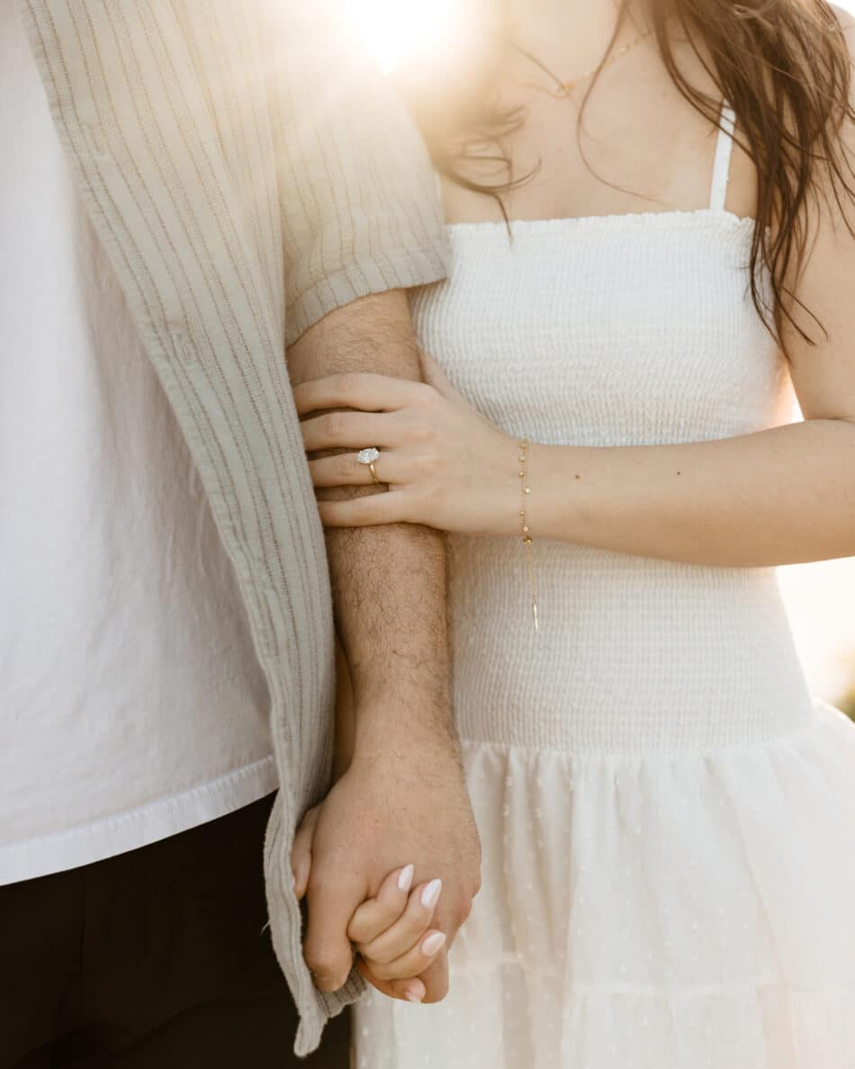 Close-up details of a gold diamond engagement ring and white dress during a luminous Malibu beach session by Erica Montgomery Photography.