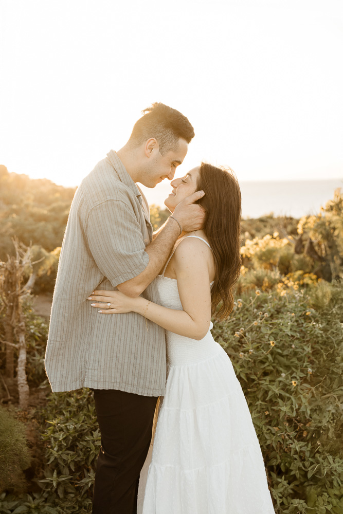 Engaged couple embracing in cliffside greenery at sunset during a Malibu engagement session by Erica Montgomery Photography.
