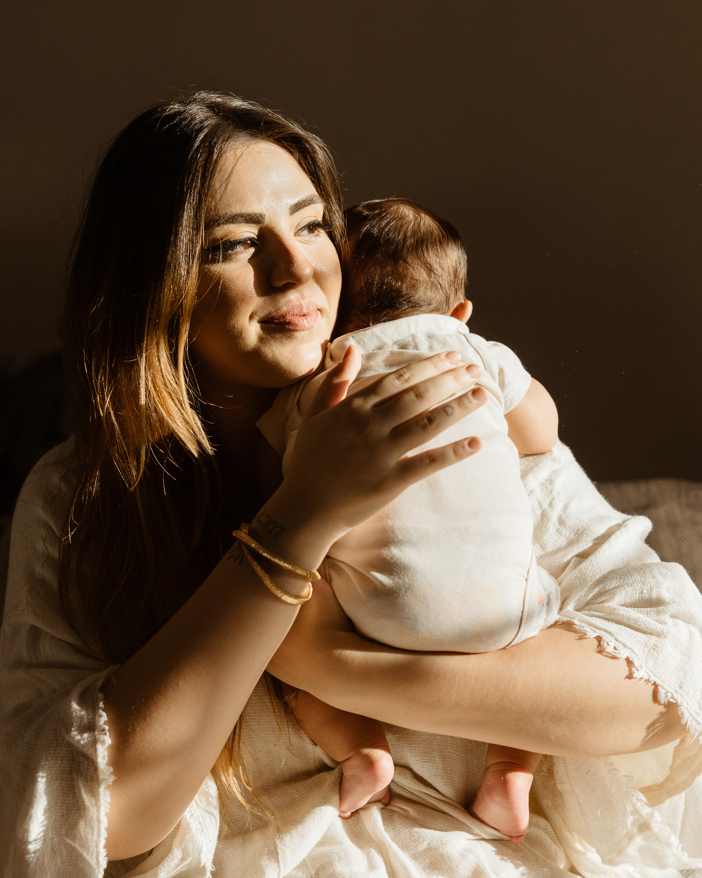 A mother gently holding and cuddling her newborn baby during an indoor lifestyle newborn photography session in Los Angeles by Erica Montgomery Photography.