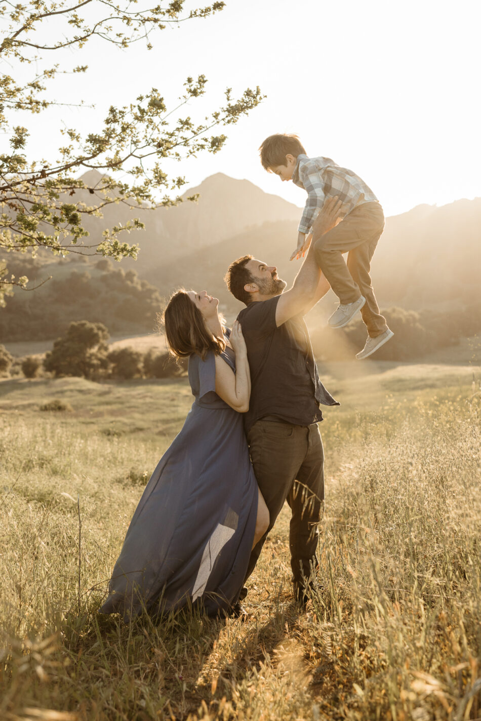 Father playfully lifting his young son in the air in a sun-drenched canyon field during a Calabasas family session by Erica Montgomery Photography.