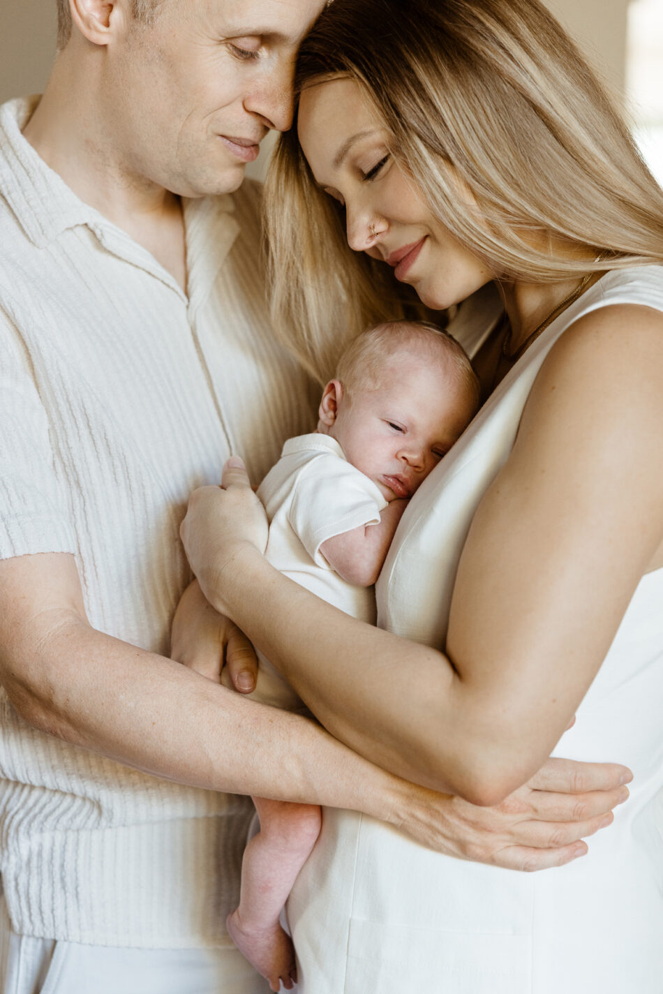 Parents tenderly embracing while holding their sleeping newborn baby during a luminous Calabasas home photoshoot by Erica Montgomery Photography.