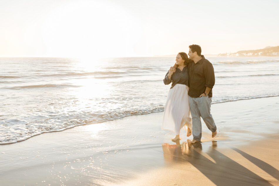 Married couple walking barefoot through glistening ocean waves at sunset during a romantic Malibu coastal photoshoot by Erica Montgomery Photography.