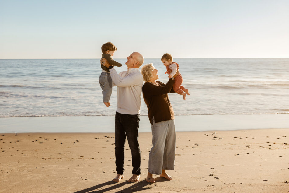 Grandparents lifting up toddlers on the shoreline during a Malibu multi-generational beach family photography session.
