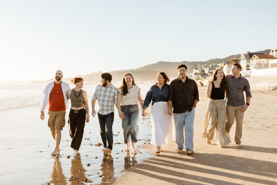 Large extended family walking hand in hand on a wet Malibu beach during a luminous golden hour photo session.
