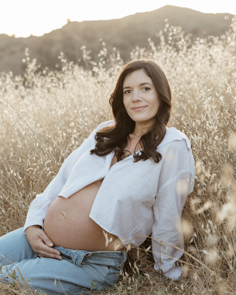 Seated solo lifestyle portrait featuring a casual style maternity look in the golden fields of Malibu Creek State Park, by Erica Montgomery.