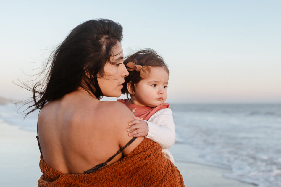 Mother holding her baby girl close on the shoreline during a coastal Malibu family portrait session by Erica Montgomery Photography.