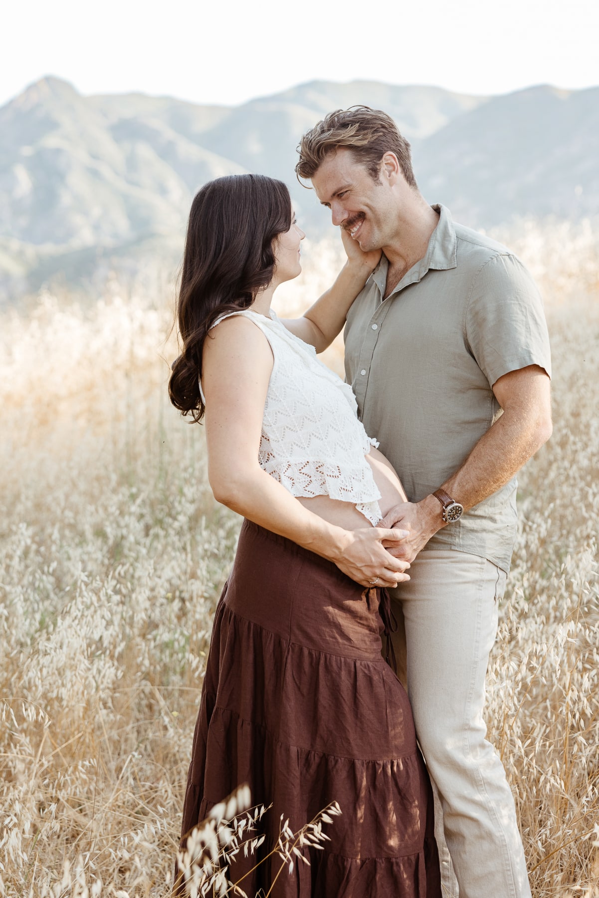 An expecting couple smiling and sharing an intimate moment during an editorial maternity photography session at Malibu Creek State Park.