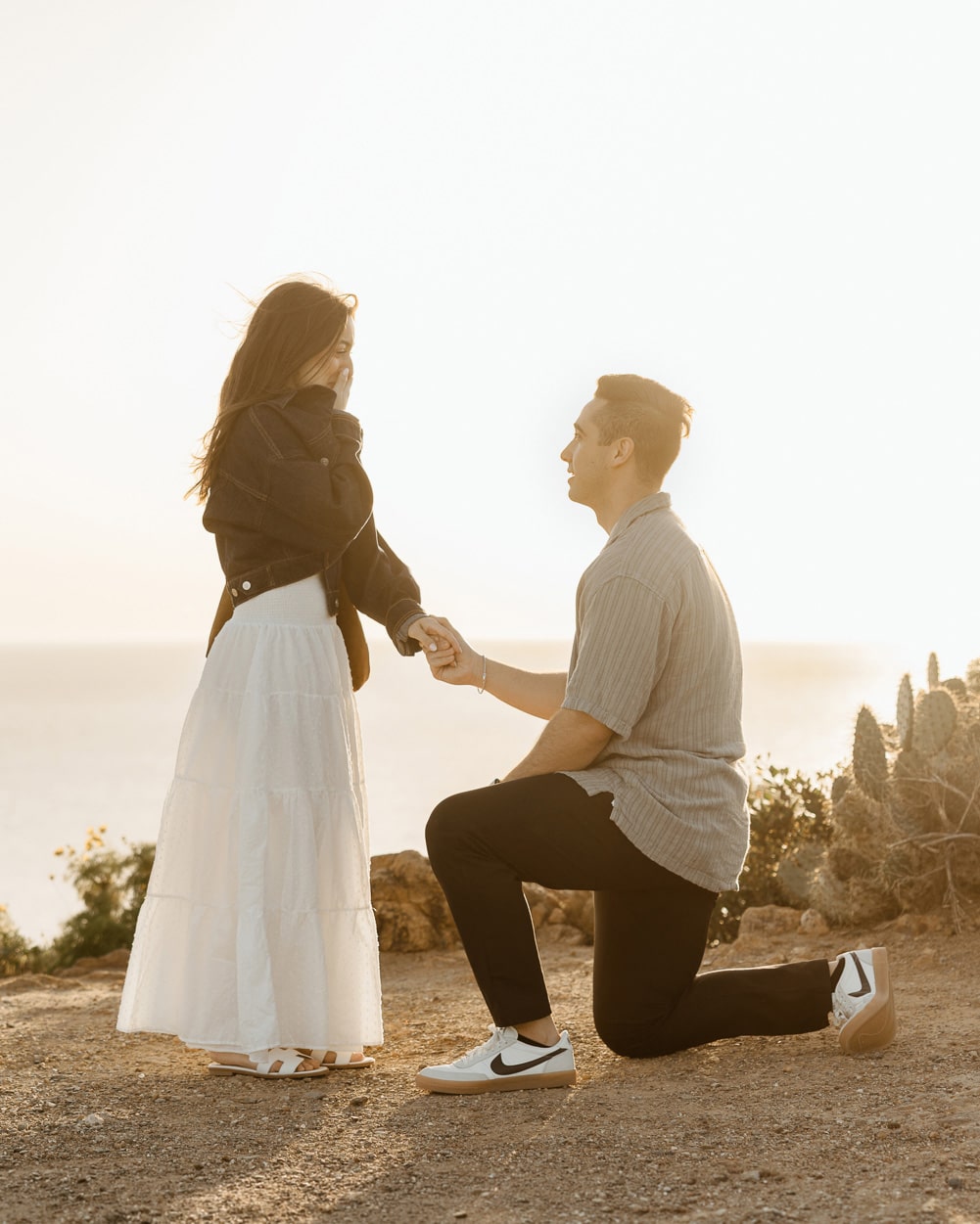 A man down on one knee proposing to his partner during a surprise beach proposal photography session at Point Dume in Malibu.